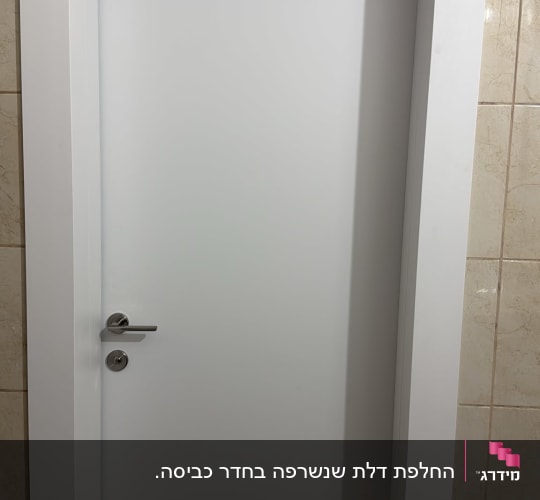דלת פנים לבנה מעוצבת עם משקוף רחב וידית כסופה מותקנת בדירה